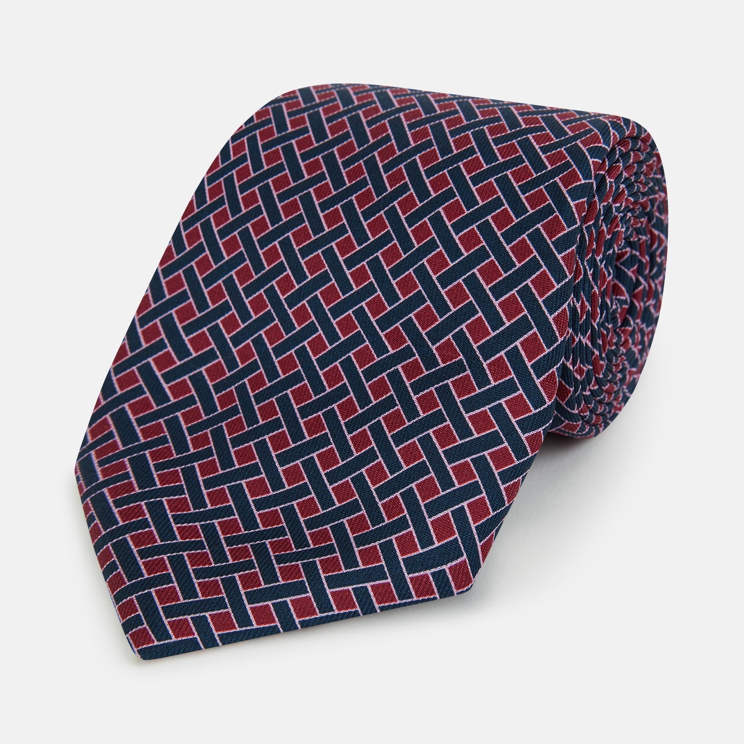 View 1 of product The Turnbull & Asser Navy and Pink Woven Printed Silk Tie features a geometric pattern with interlocking lines, displayed rolled on a light background—perfect for pairing with formal shirts.