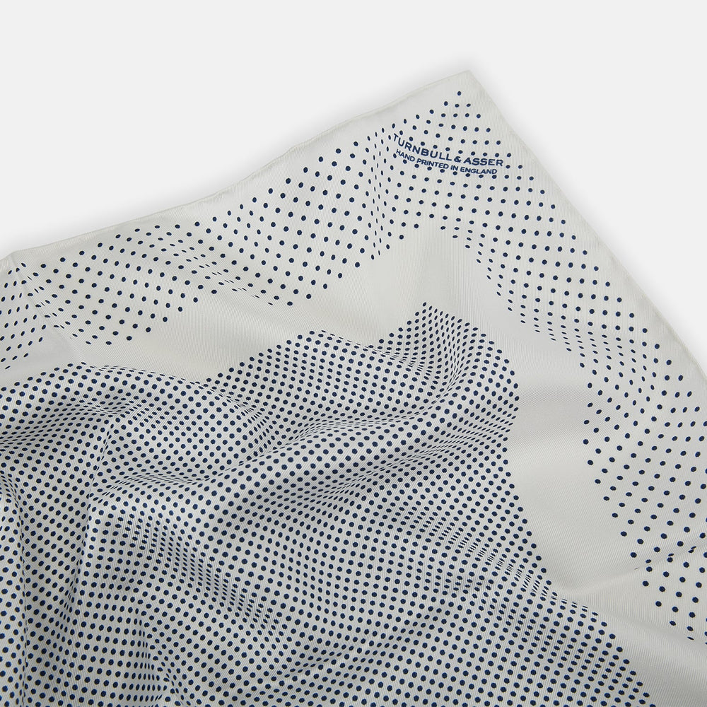 The Turnbull & Asser Cream Dot Silk Pocket Square features a neatly folded pure silk design with a border and center pattern of small navy blue polka dots, displayed on a plain white background.