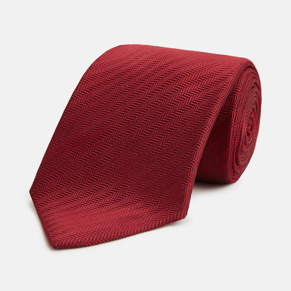 The Turnbull & Asser Plain Herringbone Burgundy Tie features a subtle pattern and rich color, making it an essential accessory for smart attire. Neatly rolled, it’s elegantly displayed on a plain white background.