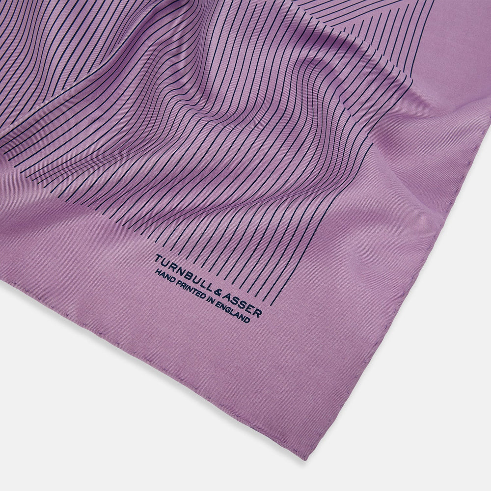 The Lilac Stripe Silk Pocket Square by Turnbull & Asser features thin vertical navy stripes on folded silk, with "TURNBULL & ASSER HAND PRINTED IN ENGLAND" inscribed in the bottom right corner, reflecting British heritage.