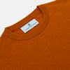 View 2 of product The Turnbull & Asser Rust Glenn Crew Neck Jumper is a plain, long-sleeved Scottish knitwear piece with ribbed cuffs and hem, shown laid flat on a white background.