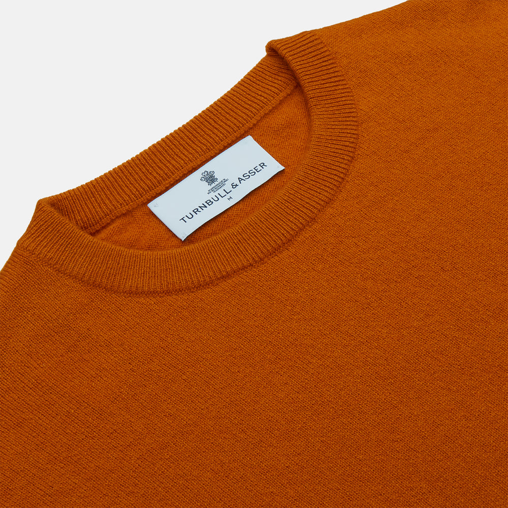 The Turnbull & Asser Rust Glenn Crew Neck Jumper is a plain, long-sleeved Scottish knitwear piece with ribbed cuffs and hem, shown laid flat on a white background.