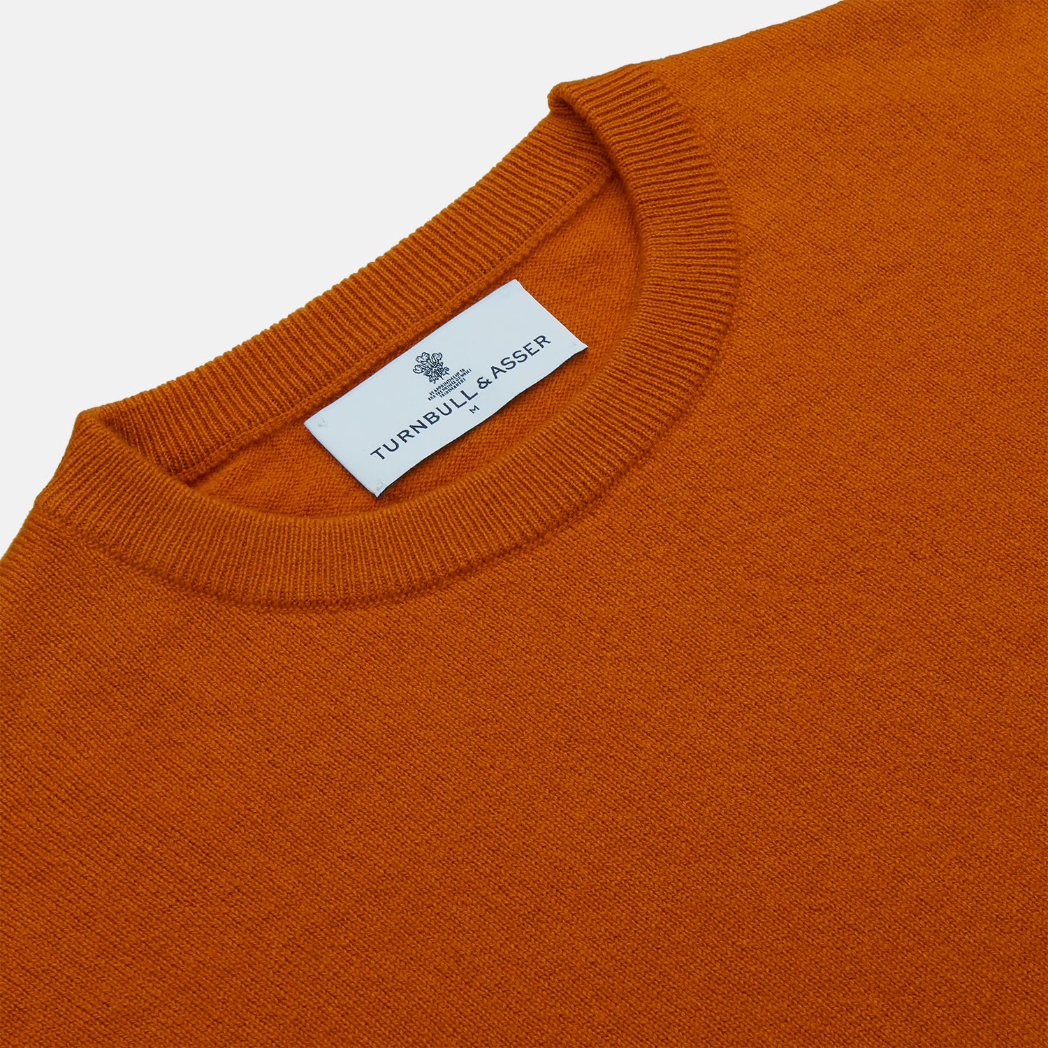 View 2 of product The Turnbull & Asser Rust Glenn Crew Neck Jumper is a plain, long-sleeved Scottish knitwear piece with ribbed cuffs and hem, shown laid flat on a white background.