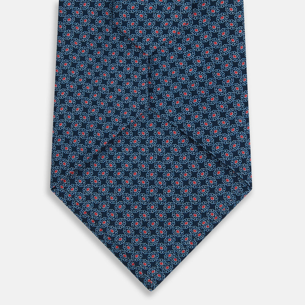 The Turnbull & Asser Navy and Red Rosette Silk Tie features a small repeating red and light blue geometric pattern on white, crafted from fine English silk.