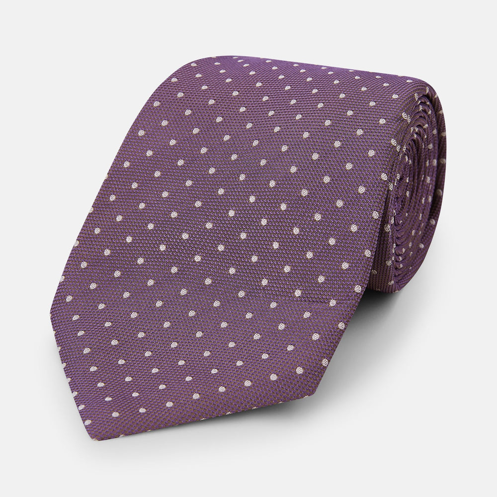The Turnbull & Asser Lilac and Purple Micro Dot Silk Tie, featuring small white dots, is a stylish accessory for smart attire. Displayed rolled-up on a light background.