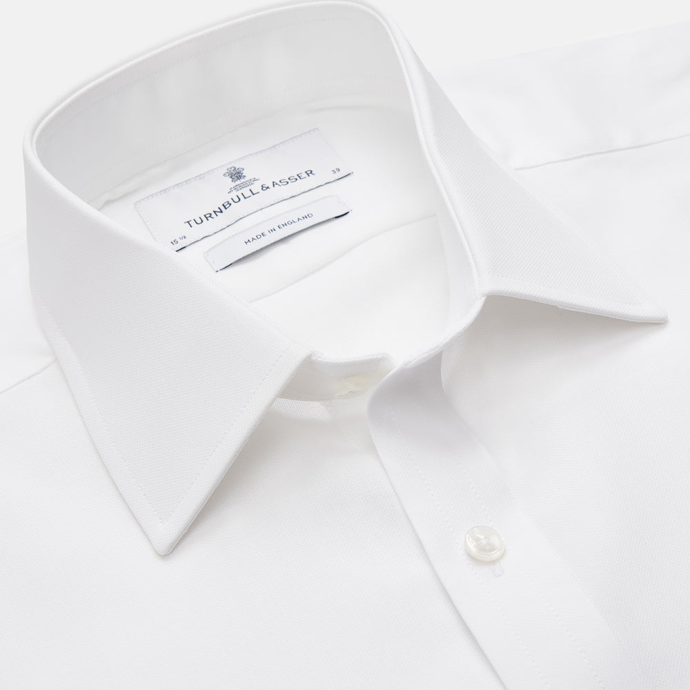 The Turnbull & Asser White Cotton Voile Regular Fit Mayfair Shirt features long sleeves, a pointed collar, button-down front, and buttoned cuffs, displayed flat against a plain white background.