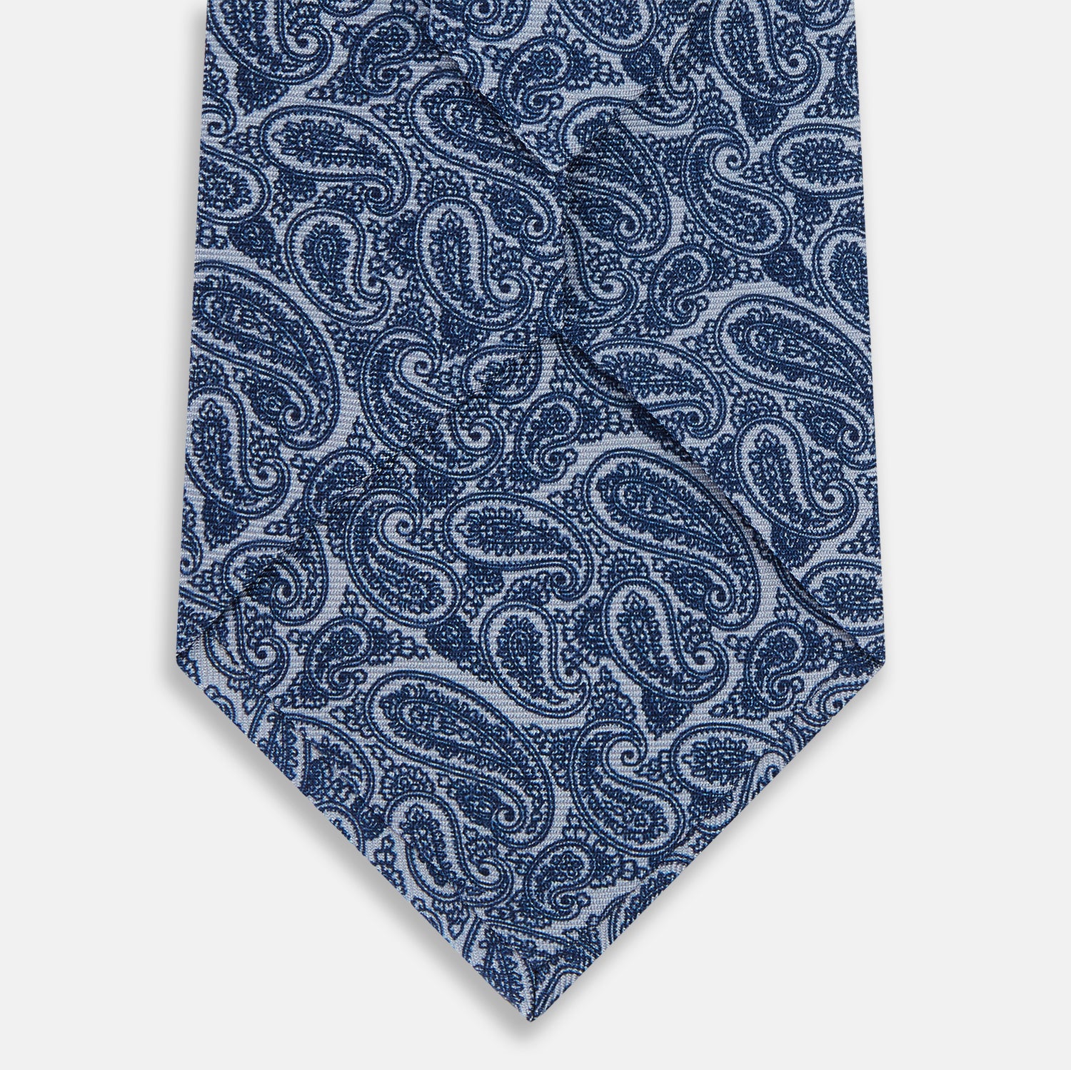 View 3 of product The Turnbull & Asser Pale Blue Paisley Silk Tie, featuring a blue paisley pattern on a pale blue background, is shown rolled up on a plain white surface.