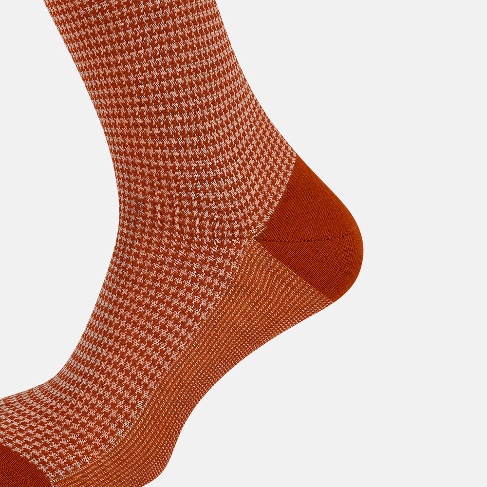 The Turnbull & Asser SOCKS LONG COTTON HOUNDSTOOTH ROSE is a single over-the-calf sock in rusty orange with a white houndstooth pattern and solid orange toe, heel, and cuff, shown on a plain white background.