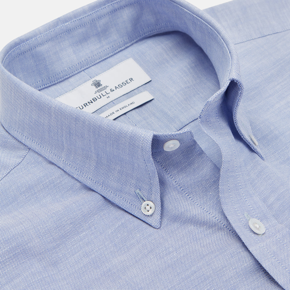 The Turnbull & Asser Mid-Blue Chambray Weekend Fit Shirt features a Dorset collar, white buttons, and 1-button cuffs. It is laid flat on a white background.