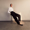 View 10 of product A woman stands in profile, looking down with hands in her pockets, wearing the Turnbull & Asser Turnbull and The Deck White Cotton Expressionist Shirt, paired with high-waisted black-and-white houndstooth pants.