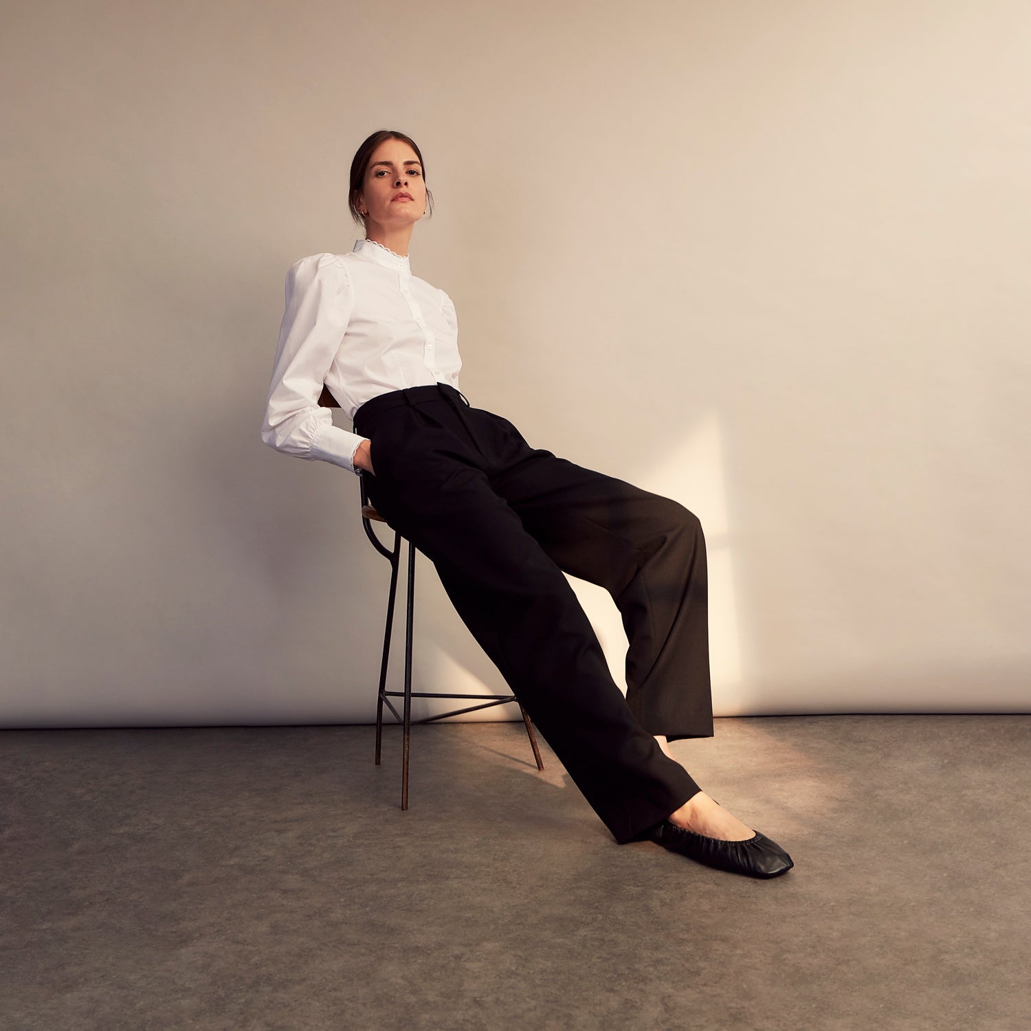View 10 of product A woman stands in profile, looking down with hands in her pockets, wearing the Turnbull & Asser Turnbull and The Deck White Cotton Expressionist Shirt, paired with high-waisted black-and-white houndstooth pants.
