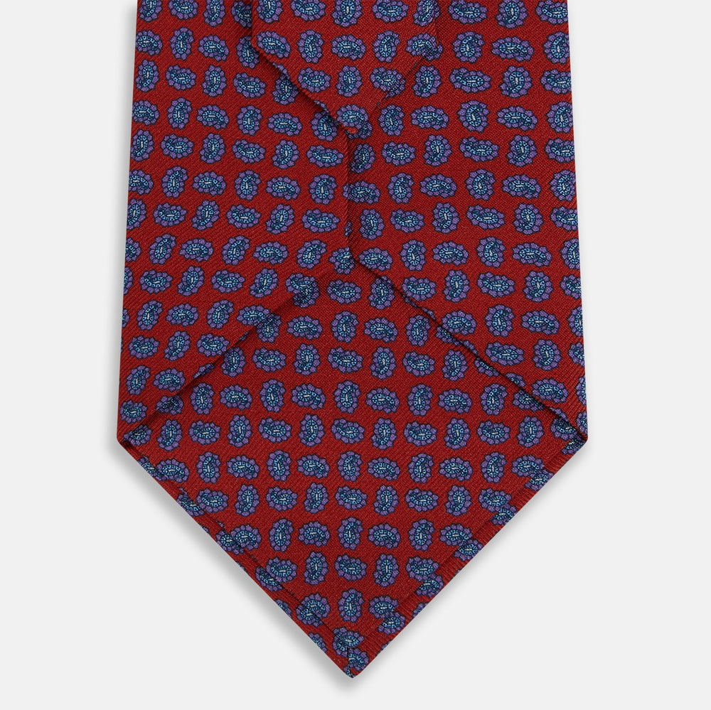 The Turnbull & Asser Red and Purple Miniature Paisley Silk Tie is neatly rolled with the pointed end facing forward.