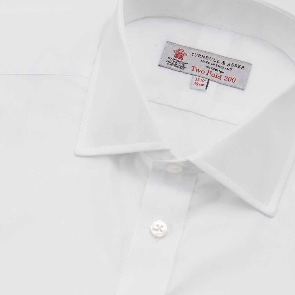 A neatly folded Turnbull & Asser Two-Fold 200 White Cotton Shirt with a Regent collar and 3-button cuffs, crafted from breathable fabric, is displayed on a light grey background with the label visible inside the collar.