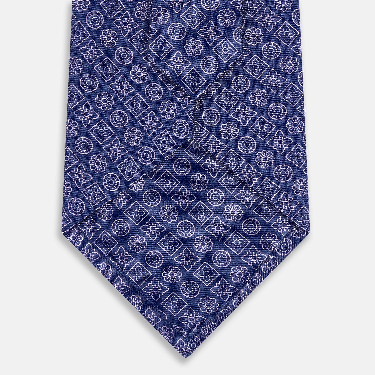 View 3 of product The Turnbull & Asser Azzurro Floral Tile Pattern Printed Silk Tie features blue silk with a geometric design of white circles, squares, and floral motifs, displayed on a plain white background.