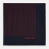 View 3 of product The Turnbull & Asser Navy and Red Stripe Silk Pocket Square features thin red stripes on navy silk, with "HAND PRINTED IN ENGLAND" in red at the corner. A folded corner shows its hand-rolled edges and refined design.