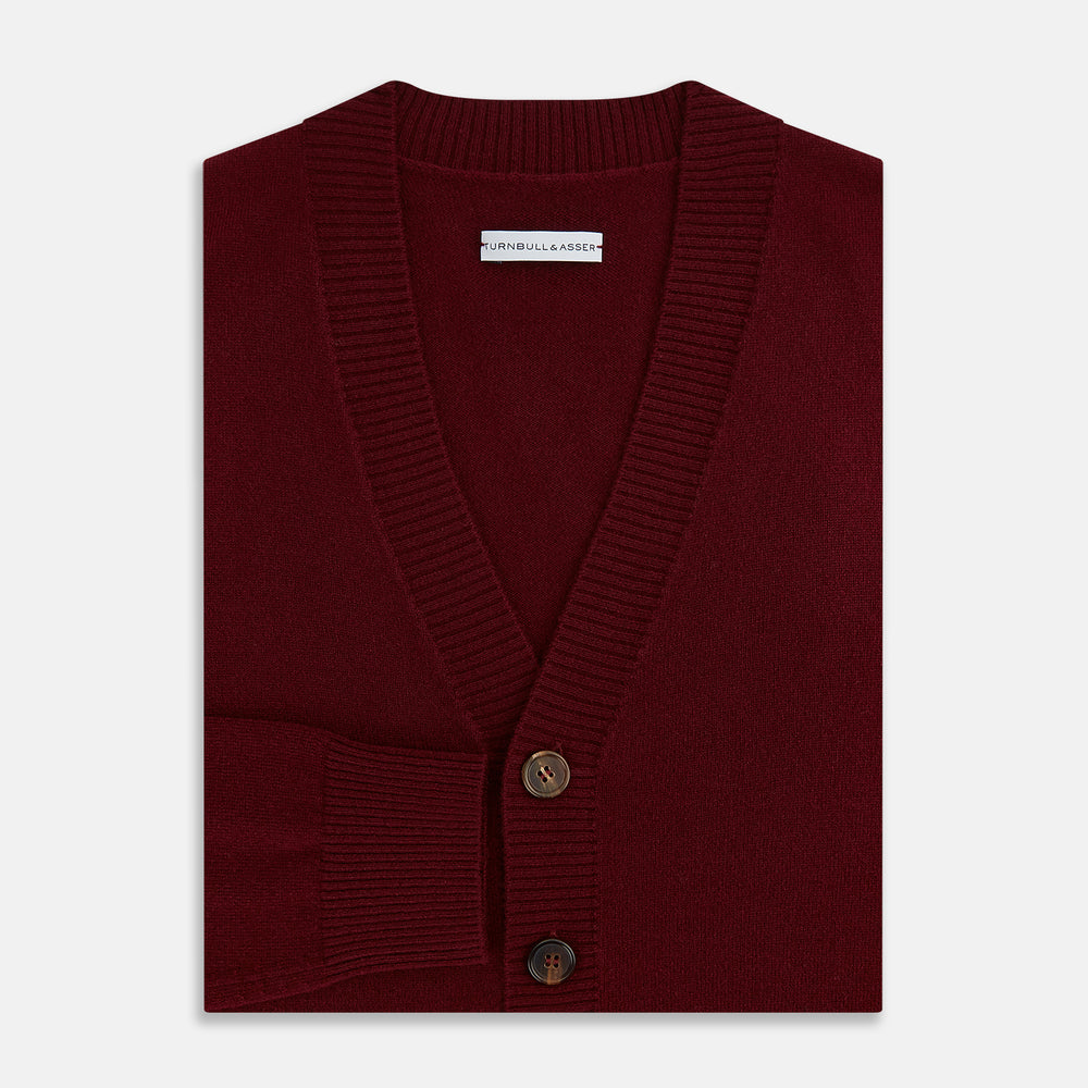 The Turnbull & Asser Burgundy Cashmere Cardigan features a V-neck, ribbed cuffs and hem, two front pockets, and a classic button-up design, shown on a plain white background.