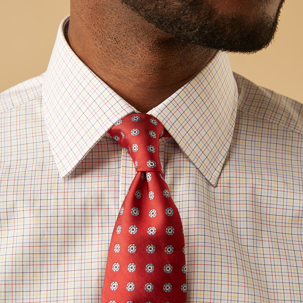 A man stands against a beige background, facing forward with a neutral expression and arms relaxed, wearing the Turnbull & Asser Red Multi Check Regular Fit Mayfair Shirt.
