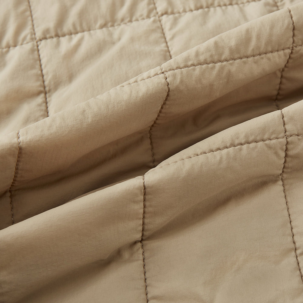 The Battersea Sand Quilted Jacket by Turnbull & Asser is a light beige men's jacket with a front zipper, pointed collar, zippered side pockets, chest pocket, and buttoned cuffs, shown on a plain white background.