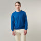 A man with light skin and short brown hair stands against a plain background, wearing the Turnbull & Asser Ocean Blue Merino Kingston Crew Neck Jumper and cream-colored pants, looking directly at the camera with a neutral expression.