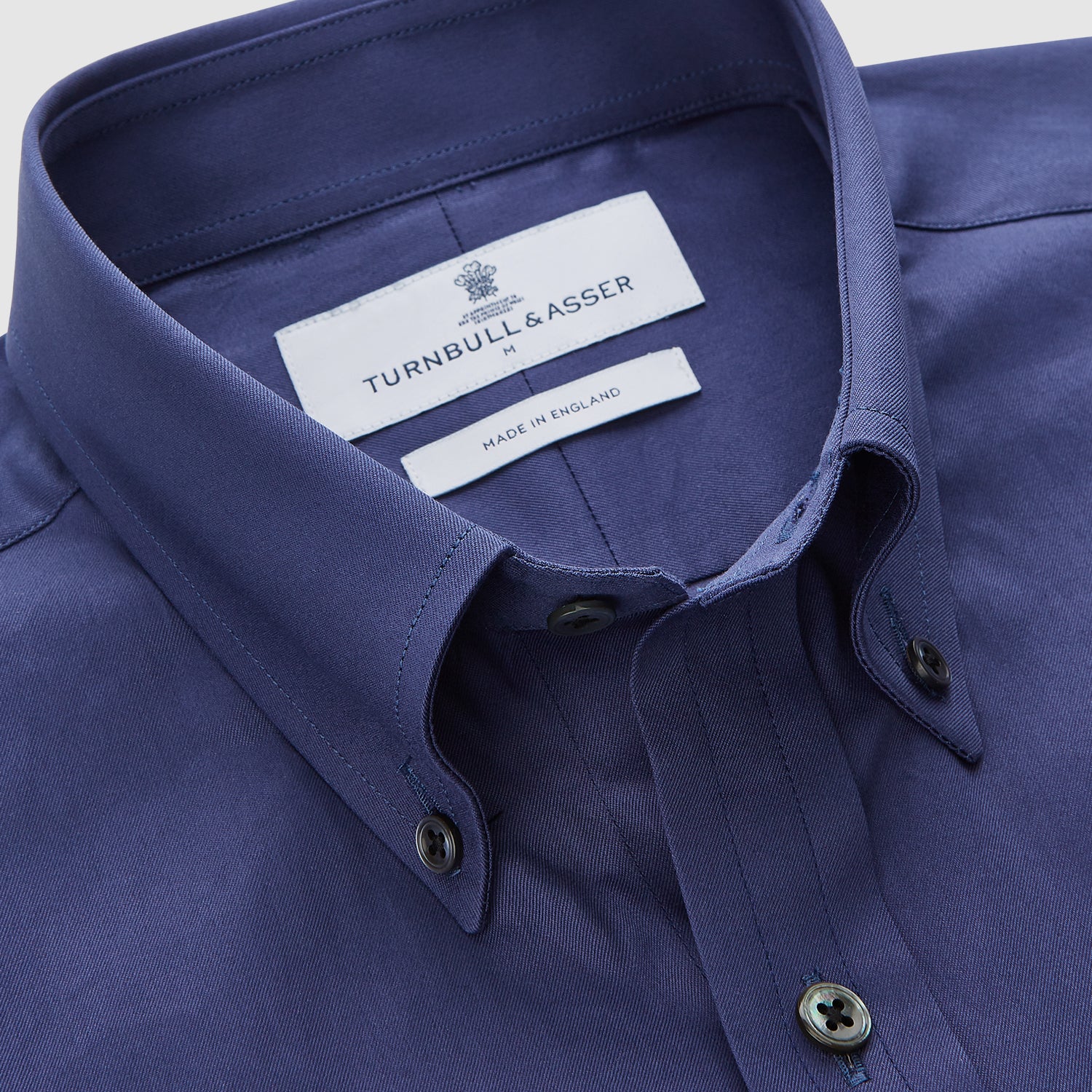 View 3 of product The Blue Piece Dyed Weekend Fit Suffolk Shirt by Turnbull & Asser features a button-down Dorset collar, chest pocket, white buttons, and long sleeves in classic navy, laid flat against a white background.