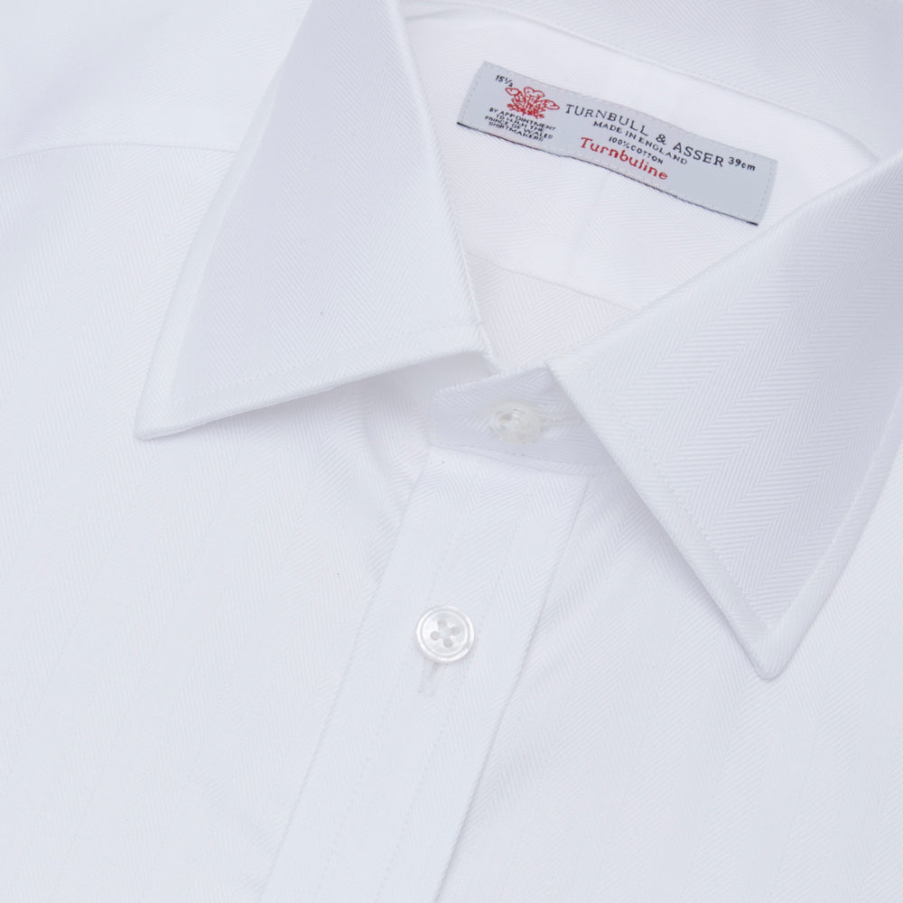 The Turnbull & Asser White Herringbone Superfine Cotton Shirt features a T&A collar, double cuffs, and a visible label inside the collar, shown neatly folded on a light blue background—ideal for minimalist looks or pairing with bold ties.