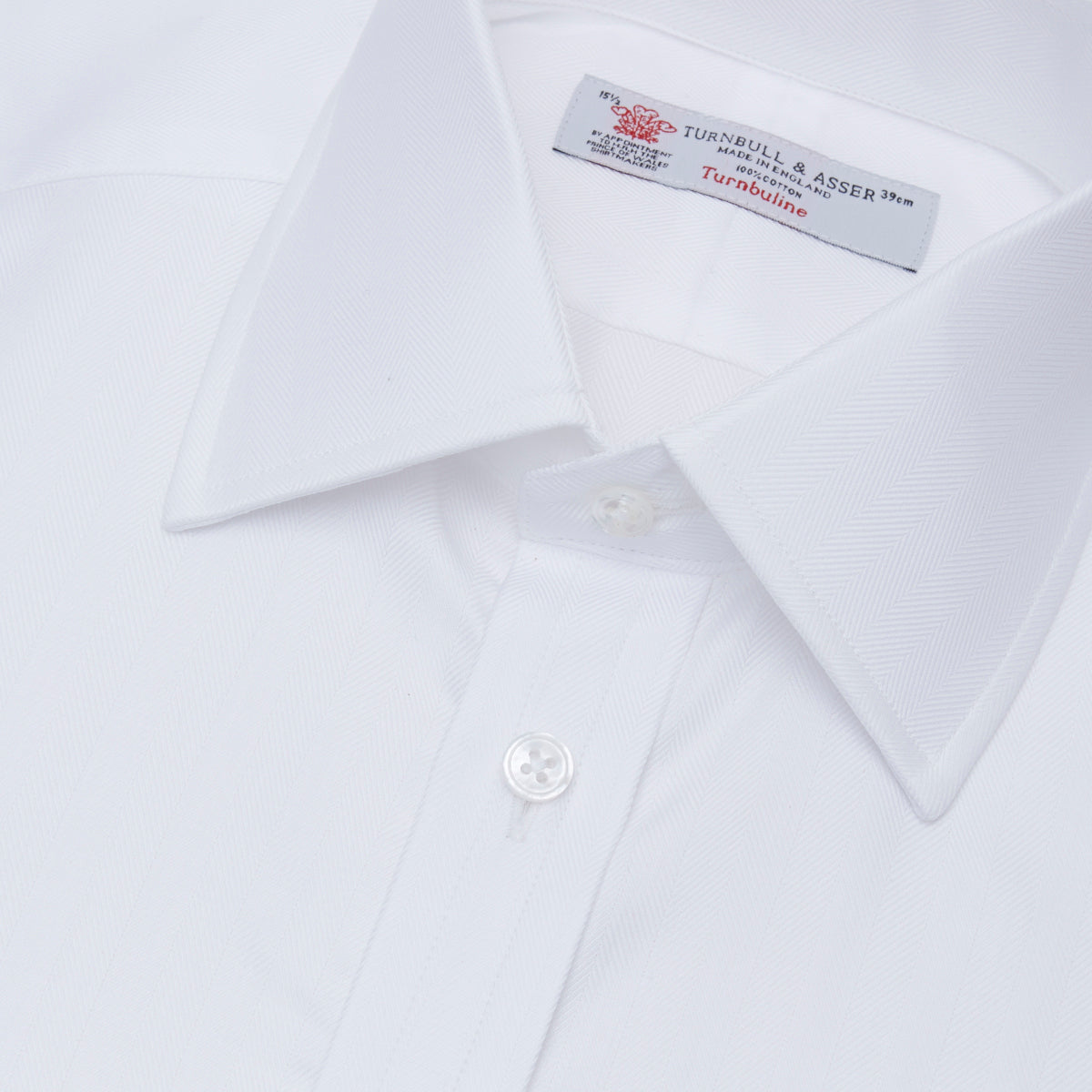 View 5 of product The Turnbull & Asser White Herringbone Superfine Cotton Shirt features a T&A collar, double cuffs, and a visible label inside the collar, shown neatly folded on a light blue background—ideal for minimalist looks or pairing with bold ties.