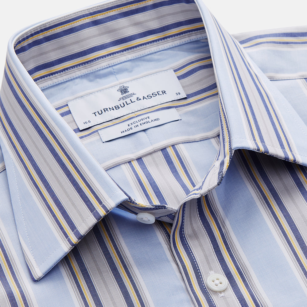 The Turnbull & Asser Pale Blue and Yellow Stripe Cotton Regular Fit Mayfair Shirt is a long-sleeve, button-down formal shirt for men, shown on a plain white background.