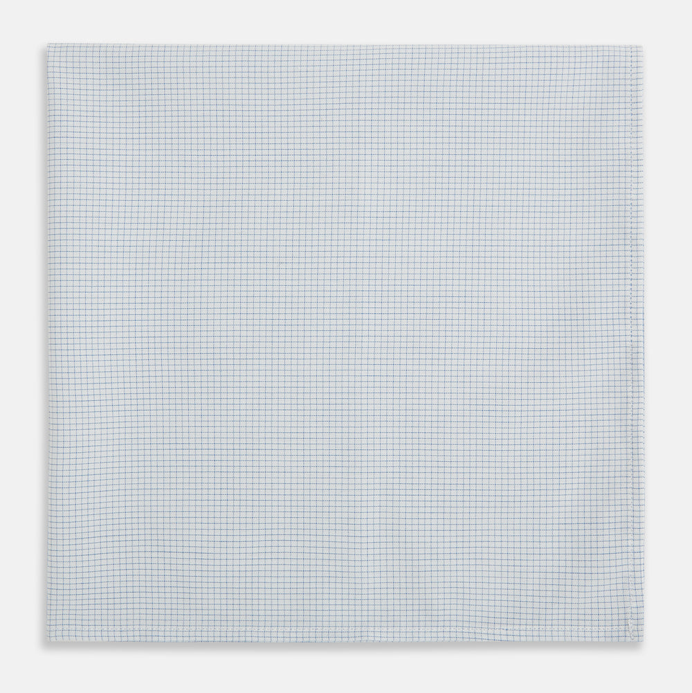 The Turnbull & Asser Hand Rolled Pale Blue Graph Check Handkerchief features a neatly folded white cotton design with a pale blue check, offering an elegant finishing touch to any setting.