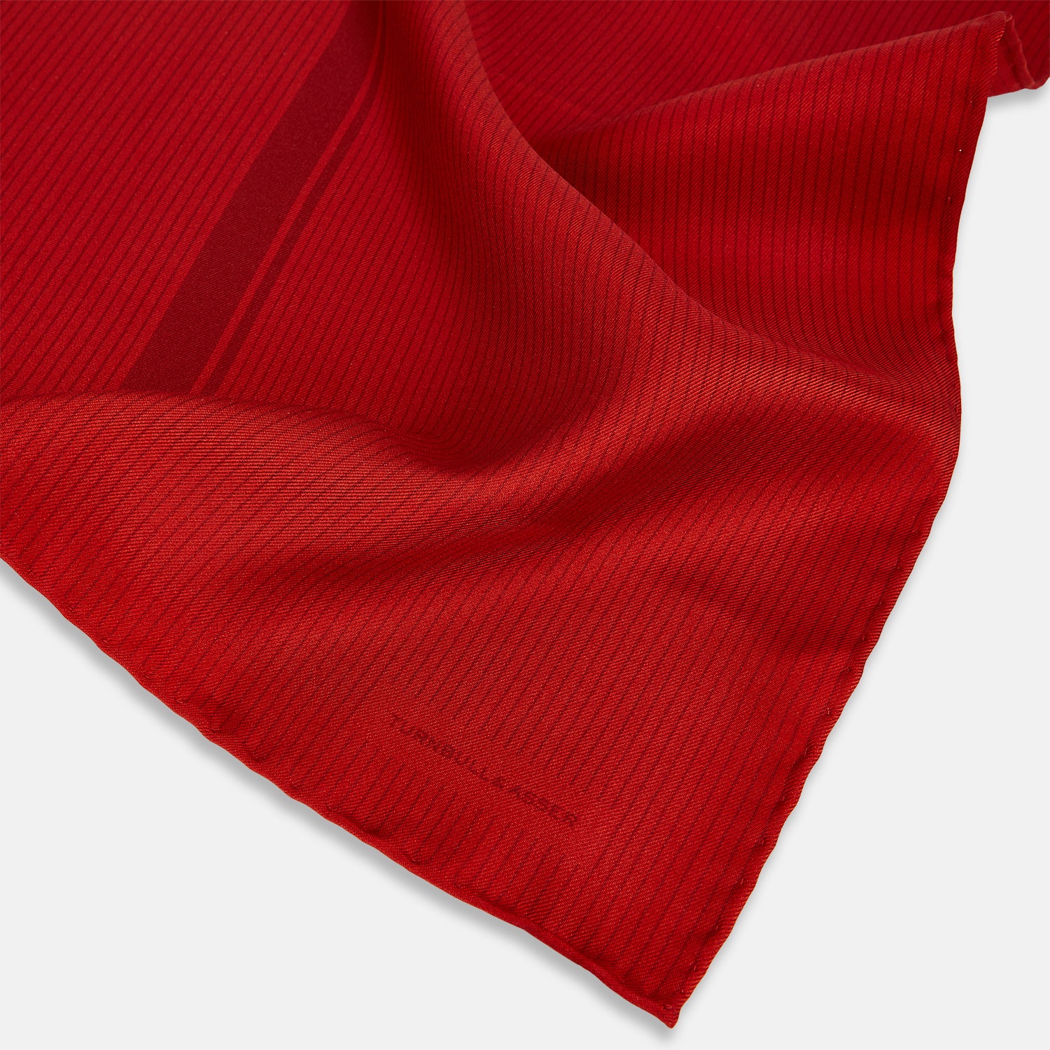 View 2 of product The Red and Burgundy Stripe Silk Pocket Square by Turnbull & Asser features subtle vertical stripes and a darker red stripe along one side, with “Turnbull & Asser” embossed in the fabric and a textured, turned-down corner.