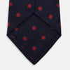 View 4 of product The EMBLEM SPOT NAVY TULIP TIE by Turnbull & Asser features a navy base with red circle motifs, neatly rolled on a white background—an essential accessory for refined style.