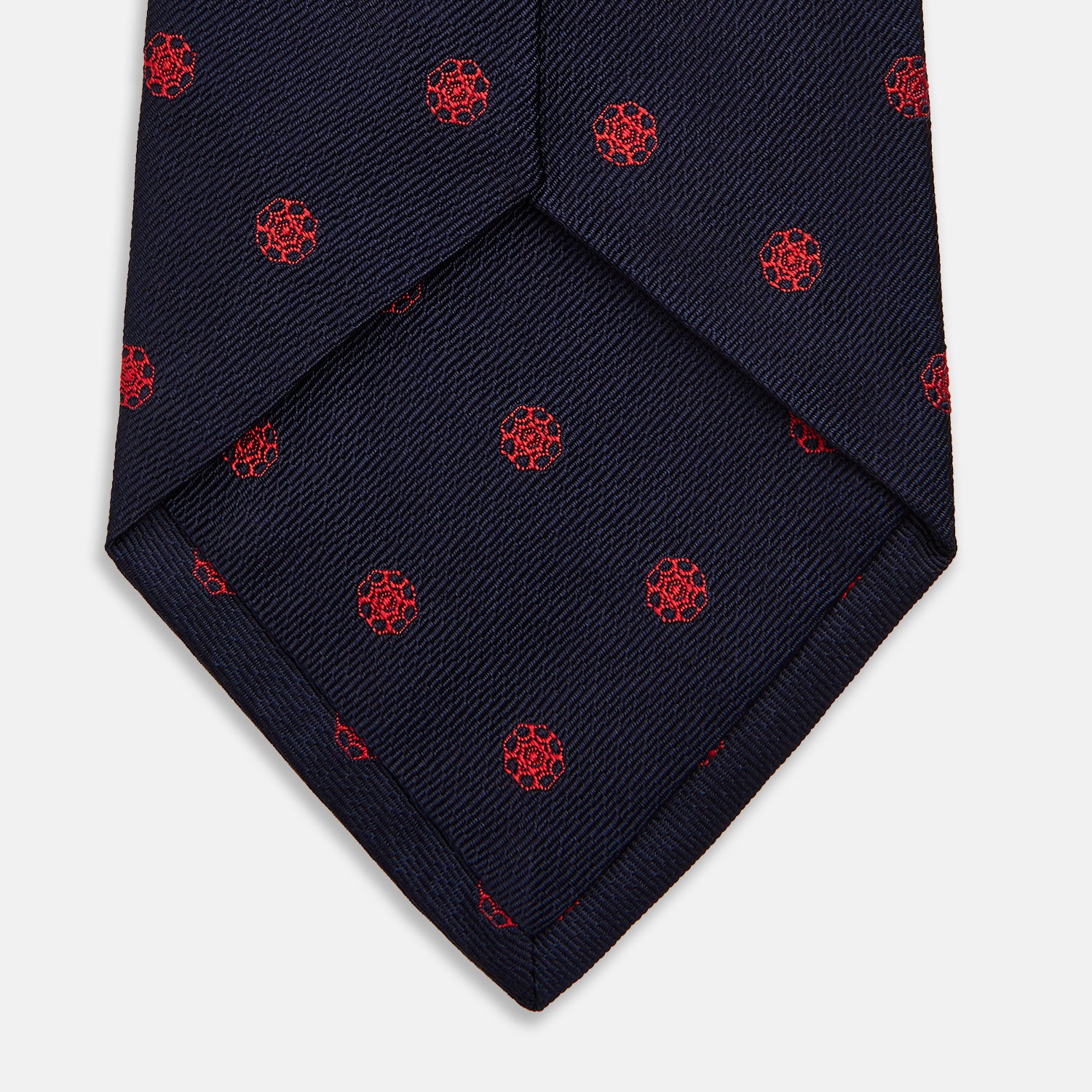 View 4 of product The EMBLEM SPOT NAVY TULIP TIE by Turnbull & Asser features a navy base with red circle motifs, neatly rolled on a white background—an essential accessory for refined style.