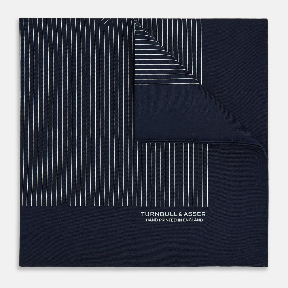 The Navy and White Stripe Silk Pocket Square by Turnbull & Asser features thin white vertical stripes and "TURNBULL & ASSER HAND PRINTED IN ENGLAND" in one corner, with a folded edge showing the reverse of this elegant silk accessory.