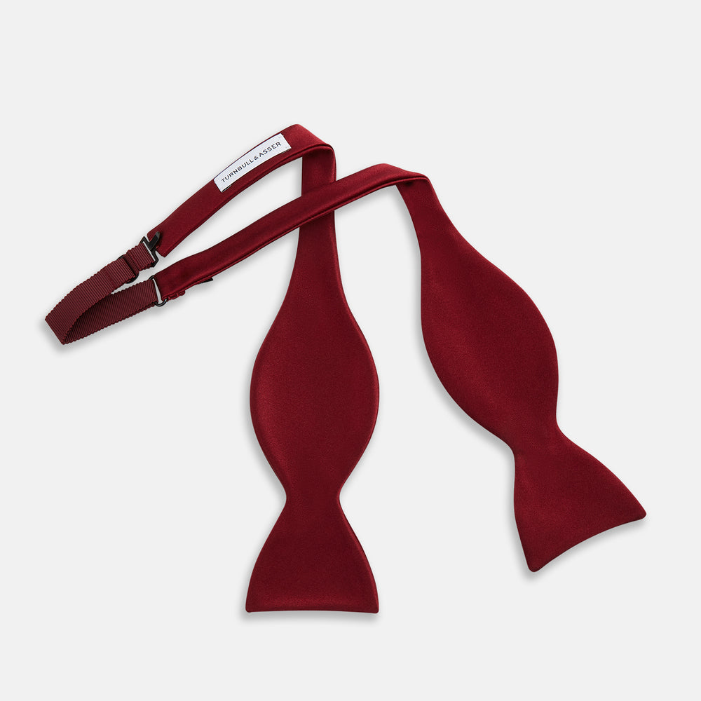 The Turnbull & Asser BURGUNDY SATIN BOW TIE features a deep red, smooth, and shiny finish—an essential accessory—neatly tied and showcased against a plain white background.