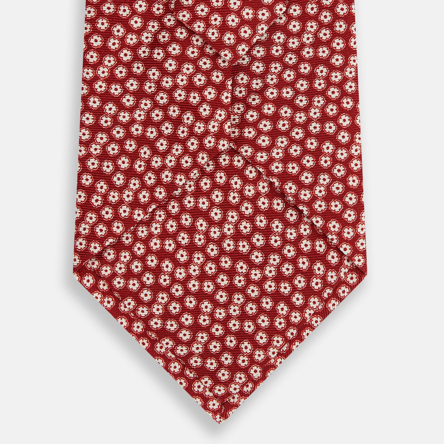 View 3 of product The Red Flower Patterned Silk Tie by Turnbull & Asser, crafted from fine English silk, features a delicate white floral design and is neatly rolled on a white background.