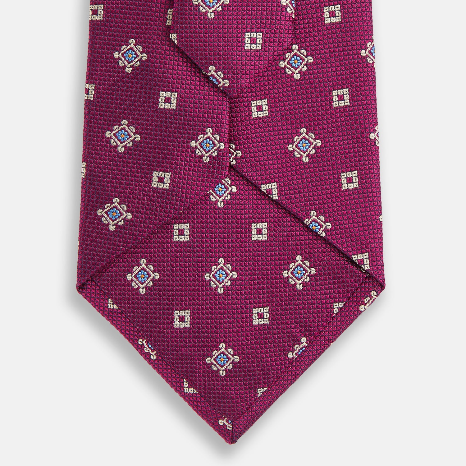 View 3 of product The Turnbull & Asser Purple Motif Silk Tie, rolled up and displayed on a light gray background, features small blue and white geometric designs—an elegant British touch for any formal event.