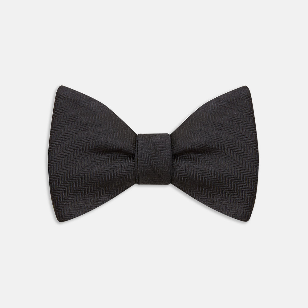 The Turnbull & Asser Black Herringbone Silk Bow Tie, ideal for formal occasions, features a subtle herringbone pattern and is shown against a plain white background.
