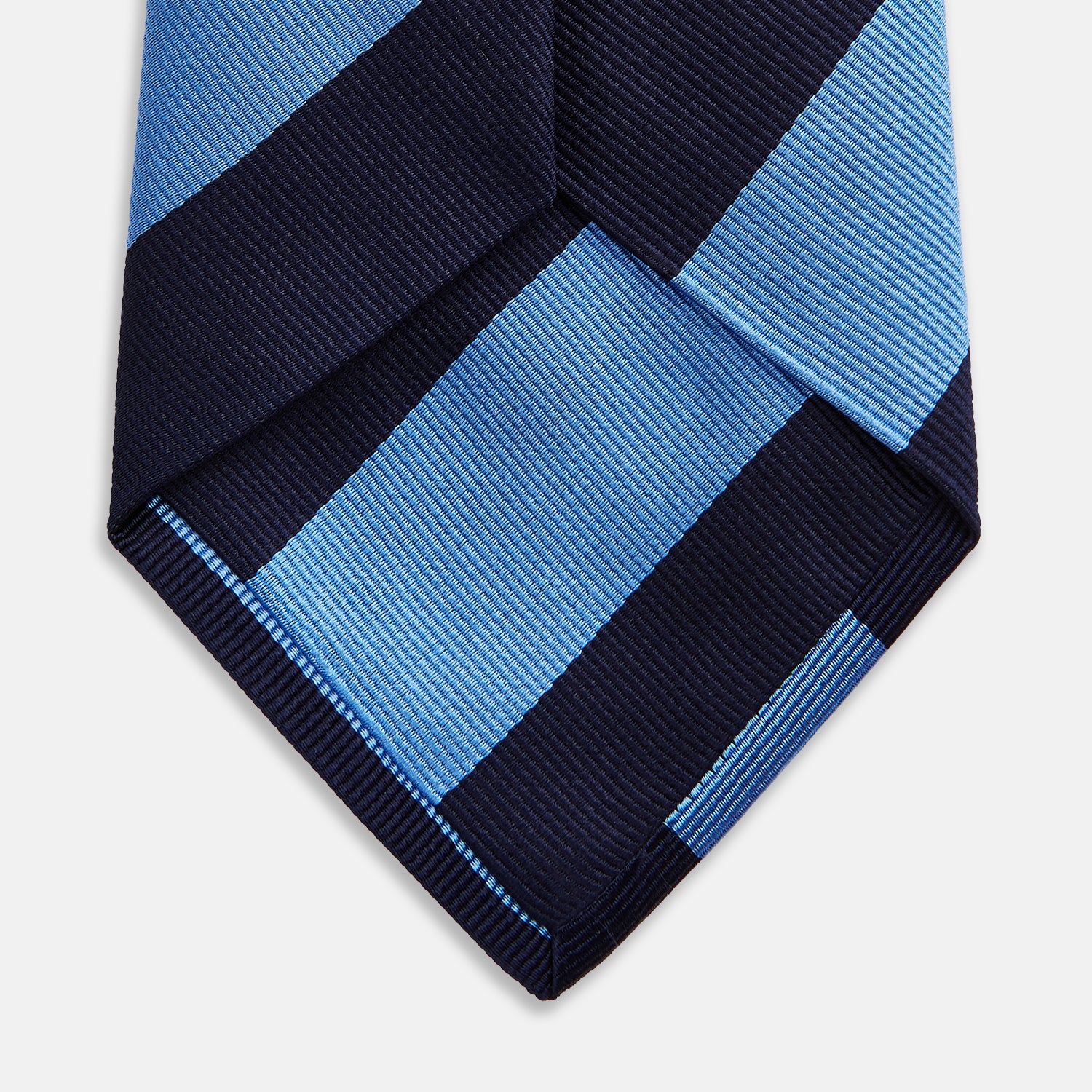 View 4 of product The BLOCK STRIPE NAVY RIVER TIE by Turnbull & Asser features bold navy and light blue diagonal stripes, rolled up neatly on a white background—a stylish essential for elevating any formal look.