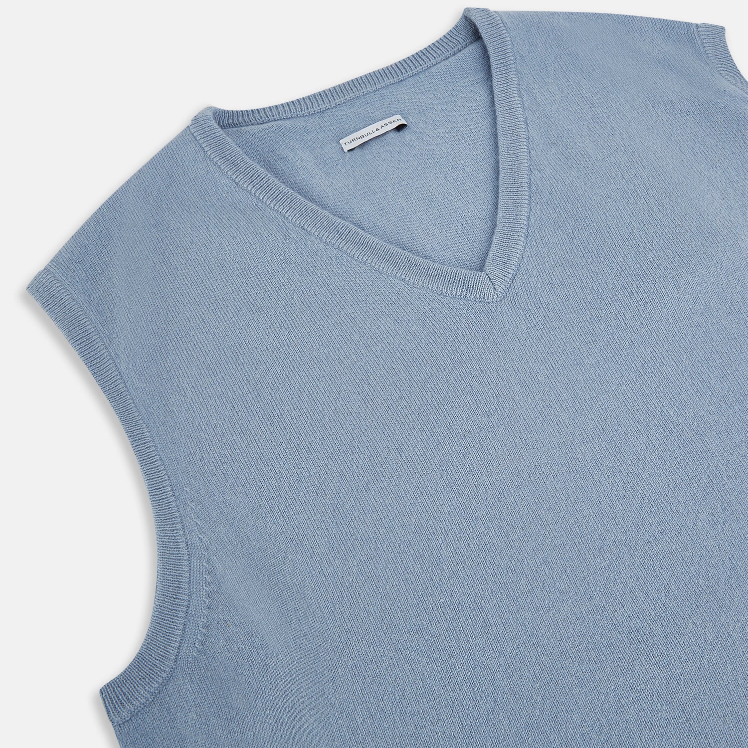 View 2 of product The Frost Blue Cashmere V-neck Vest by Turnbull & Asser features a sleeveless knit design and ribbed edges, shown on a white background—a sophisticated addition to gentleman’s fashion.