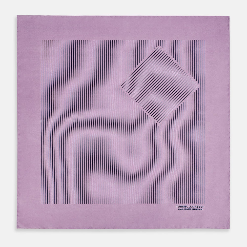 The Lilac Stripe Silk Pocket Square by Turnbull & Asser features thin vertical navy stripes on folded silk, with "TURNBULL & ASSER HAND PRINTED IN ENGLAND" inscribed in the bottom right corner, reflecting British heritage.