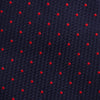 View 3 of product The Turnbull & Asser LACE ON TONE SPOT NAVY TULIP RED TIE is a classic men's accessory crafted from textured navy fabric with small red polka dots, neatly rolled with the pointed end facing forward.