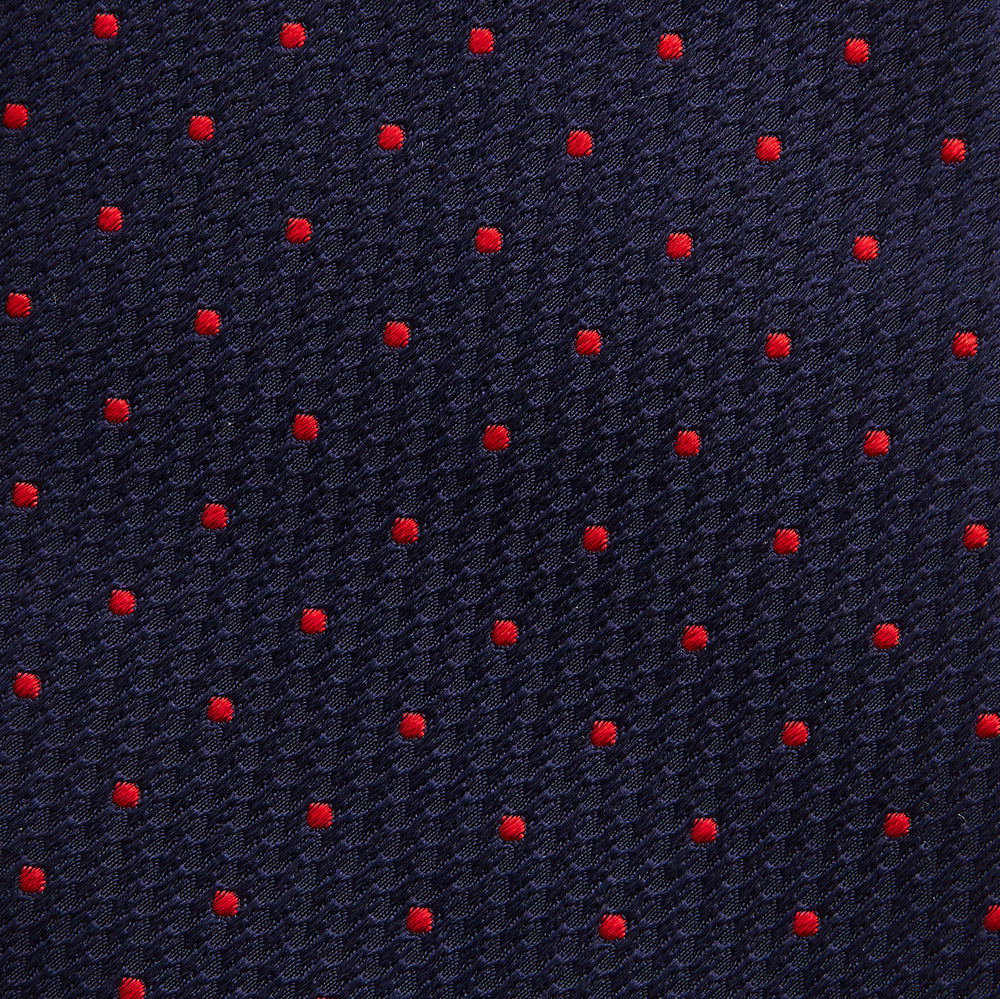 The Turnbull & Asser LACE ON TONE SPOT NAVY TULIP RED TIE is a classic men's accessory crafted from textured navy fabric with small red polka dots, neatly rolled with the pointed end facing forward.