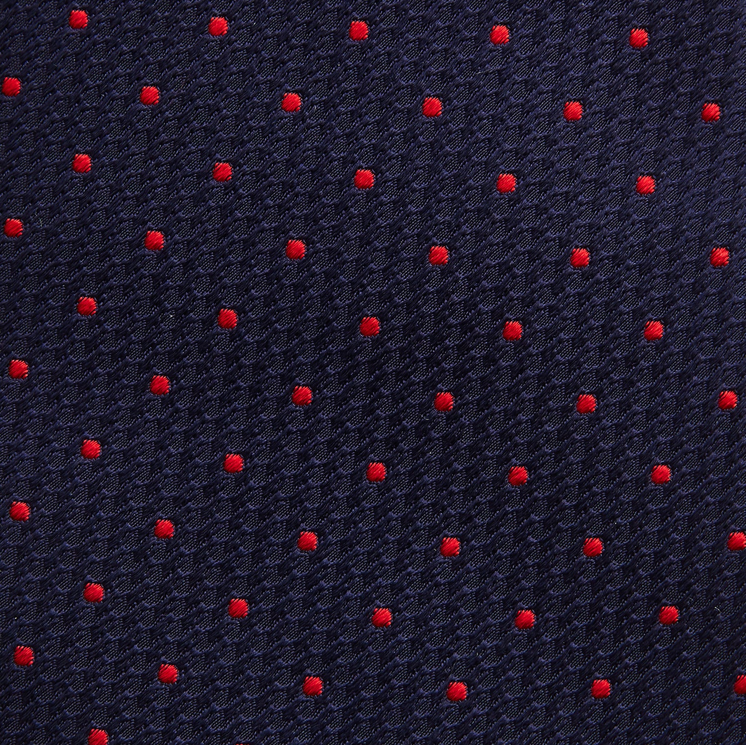 View 3 of product The Turnbull & Asser LACE ON TONE SPOT NAVY TULIP RED TIE is a classic men's accessory crafted from textured navy fabric with small red polka dots, neatly rolled with the pointed end facing forward.