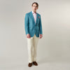 View 5 of product A man with short brown hair and a neutral expression stands against a plain background, wearing a Teal Linen Barrington Blazer by Turnbull & Asser, a light pink dress shirt, white trousers, brown loafers, and a patterned pocket square.