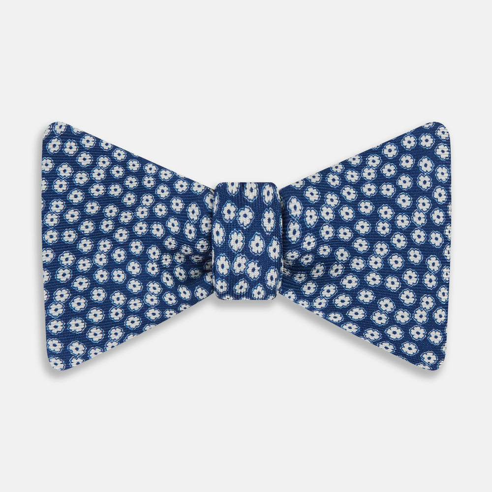 The Azzurro Flower Patterned Silk Bow Tie by Turnbull & Asser features small white flowers on blue silk, creating a refined accessory for smart attire. Shown against a white background.