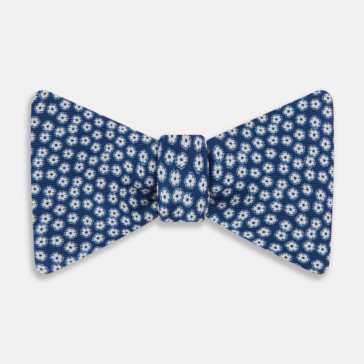 View 1 of product The Azzurro Flower Patterned Silk Bow Tie by Turnbull & Asser features small white flowers on blue silk, creating a refined accessory for smart attire. Shown against a white background.