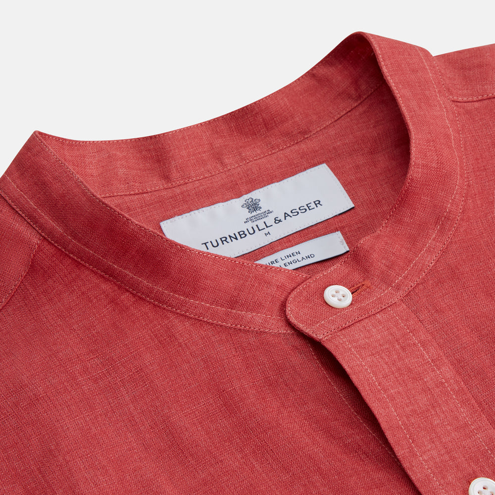 The Turnbull & Asser Plain Red Linen Weekend Fit Shirt with Stand Collar features long sleeves, a button-up front, and two buttoned-flap chest pockets. It is shown neatly laid flat on a plain light background.