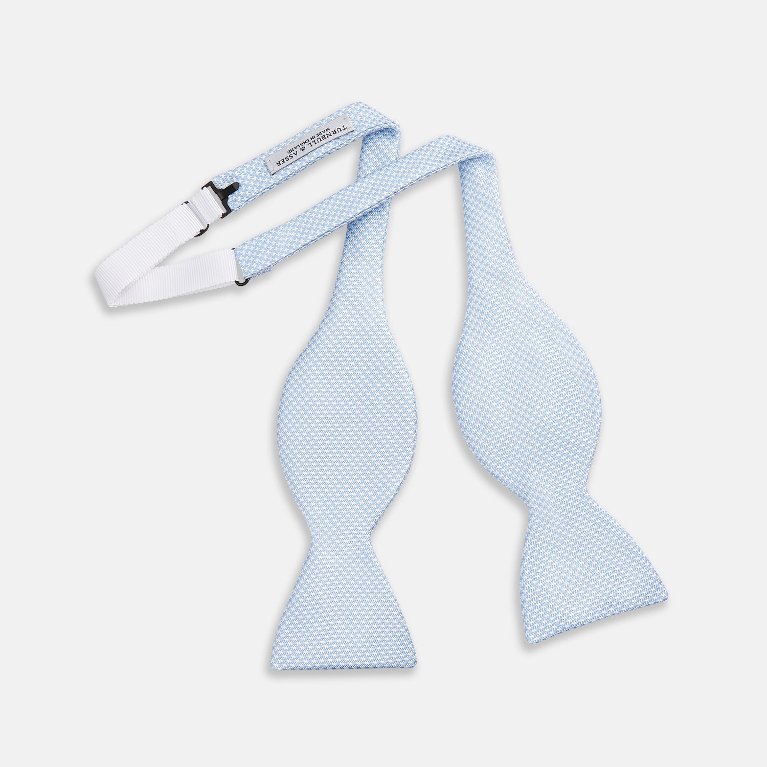 View 2 of product The Turnbull & Asser Pale Blue and White Houndstooth Silk Bow Tie features a refined textured pattern, making it an elegant formalwear accessory against a crisp white background.