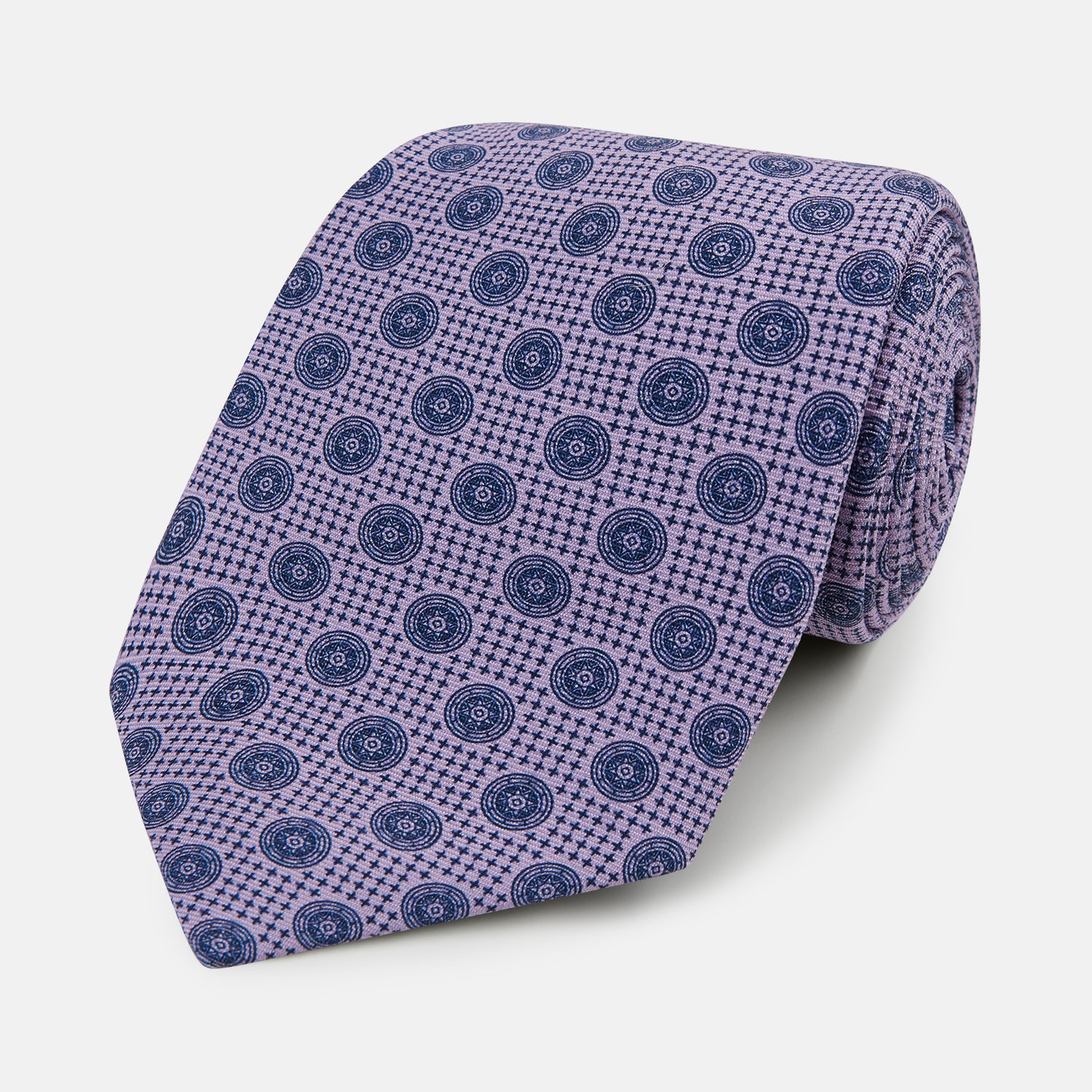 View 1 of product The Turnbull & Asser Lilac Medallion Silk Tie features a repeating navy medallion motif on textured lilac silk, adding refined style to any ensemble.