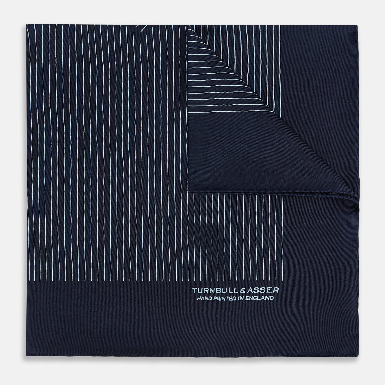 View 1 of product The Turnbull & Asser Navy and Light Blue Stripe Silk Pocket Square features hand-rolled edges and "Turnbull & Asser Hand Printed in England" in white text.