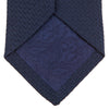 View 4 of product The Turnbull & Asser Navy Plain Woven Grenadine Silk Tie, an essential accessory, is rolled at one end and displayed on a plain white background.